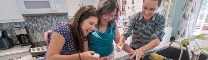 Two international students laugh with Homestay host while preparing a meal