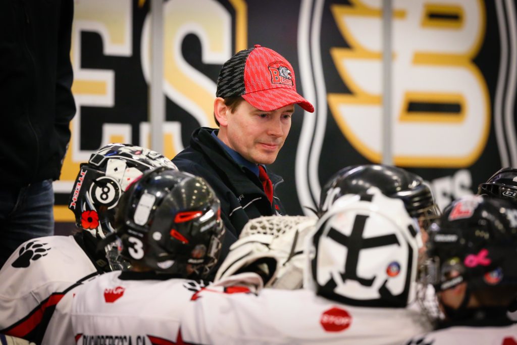 A person stands in the centre of a group of people dressed in hockey uniforms.