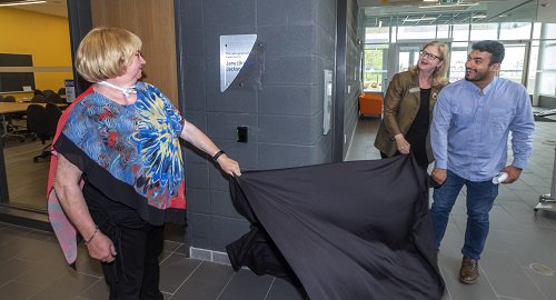Person pulls a cloth off a plaque while two others watch.