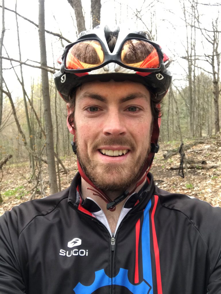 Person wearing a bike helmet stands outside and smiles at the camera.