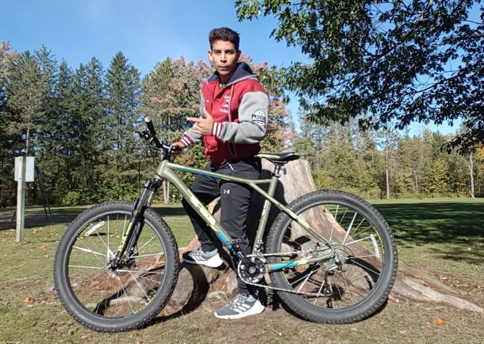 Person stands outside behind a bike they are holding up.