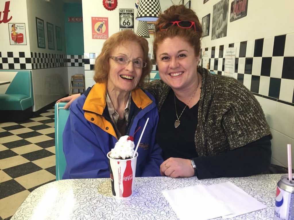 Two people sit on the same side of a diner booth and smile at the camera.