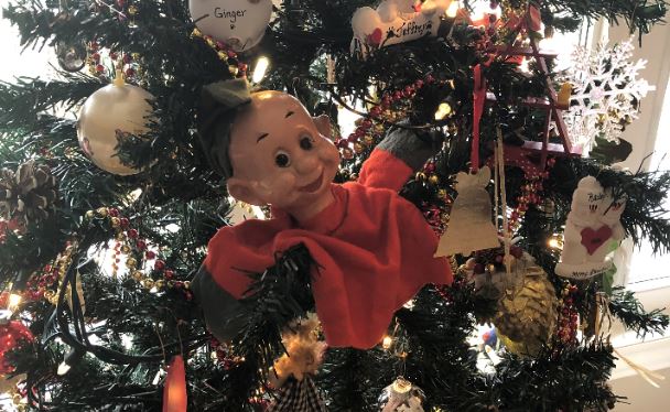 A puppet sits on the branches of a Christmas tree.