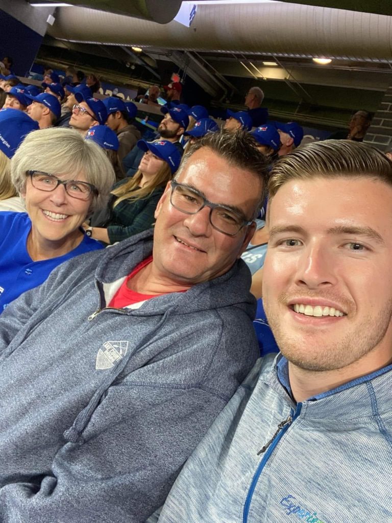 Three people take a selfie together sitting in stadium seats at a Toronto Blue Jays game.