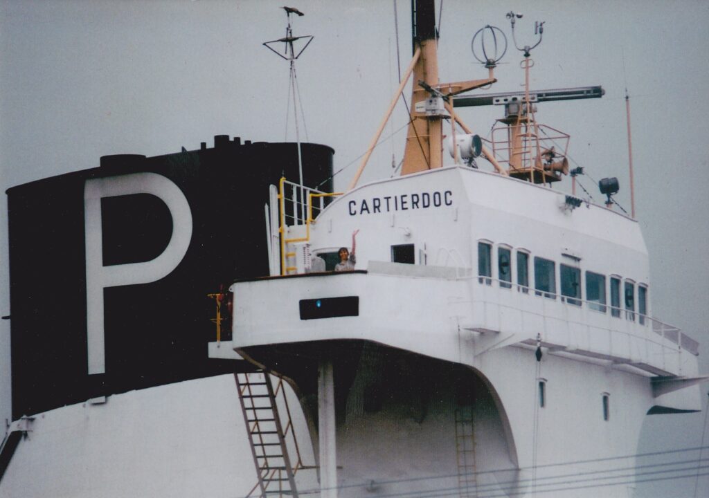 A woman stands waving on a ship.