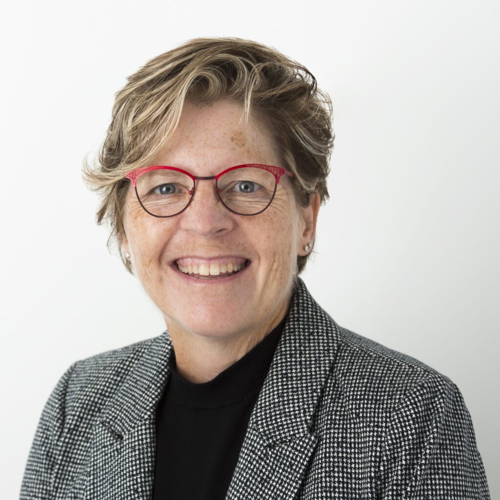 Lisa Bertram, a Civil Engineering Technology and Civil Engineering Technician alumna of Georgian College. She's smiling broadly at the camera and is wearing her blond hair short. She's wearing reddish pink glasses and a grey suit jacket with black top.