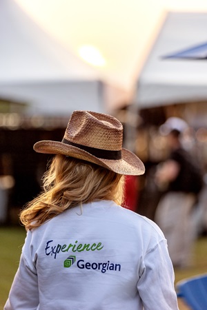 Tall Pines Festival - young woman in cowboy hat facing away from camera wearing sweatshirt with Experience Georgian on the back