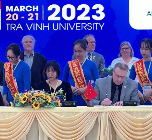Kevin Weaver (right), President and CEO, Georgian College, signs an MOU with Khoi Nguyen Investment Group (KNI) in Vietnam to advance internationalization and innovative global partnerships, alongside Ms. Thao Trinh (left), Deputy General Director and member of the KNI Board of Directors. Seated at table signing with people behind them
