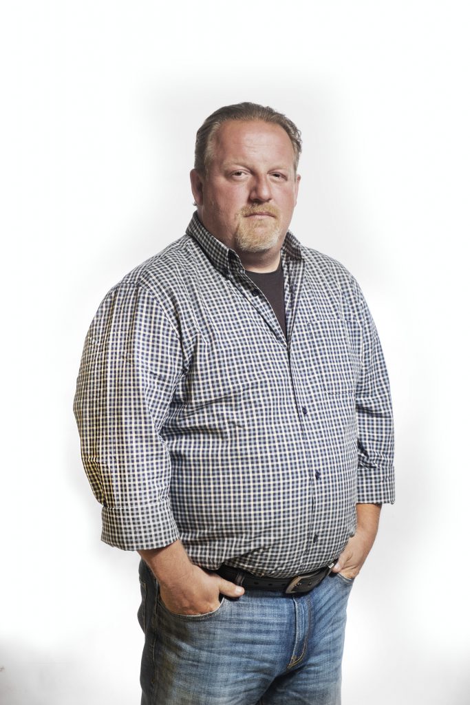 A person stands with their hands in their front pant pockets and looks at the camera.