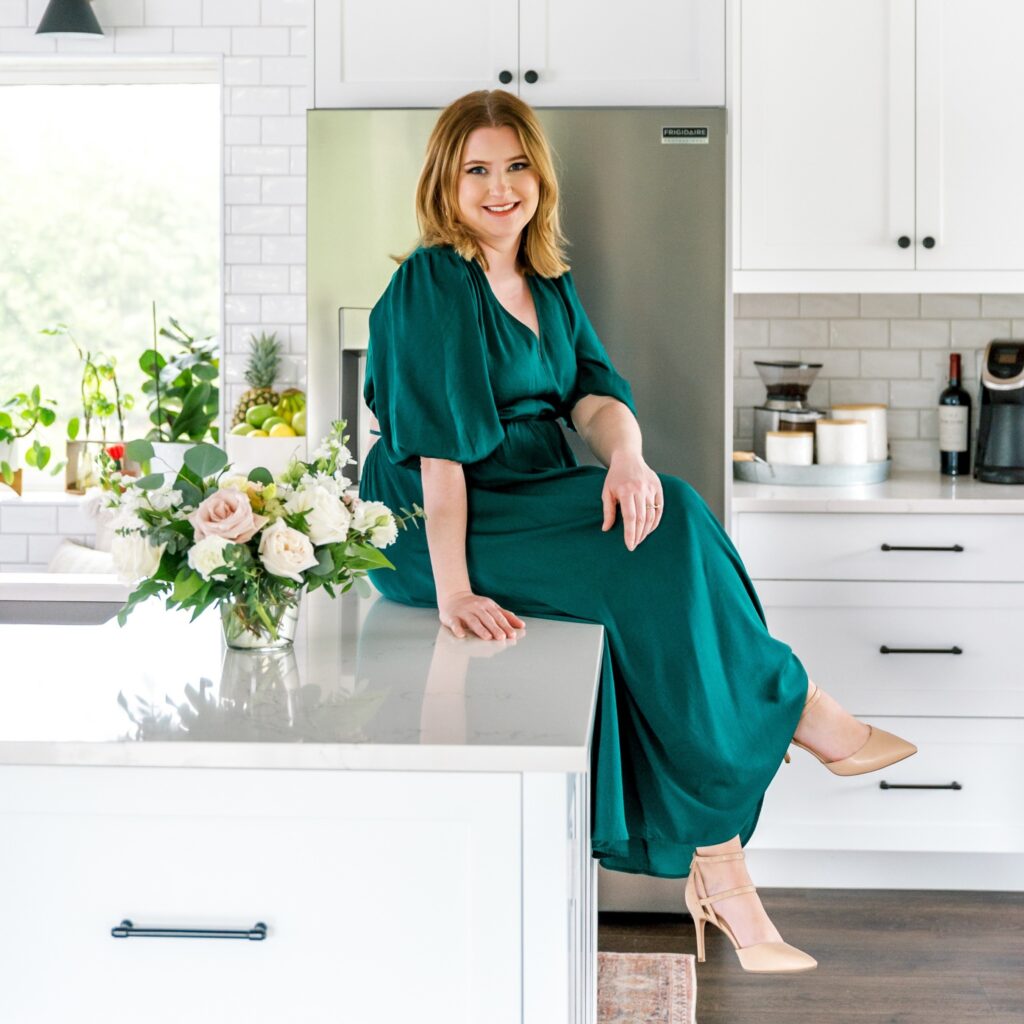 Markie Tuckett, an alumna of Georgian’s Interior Decorating diploma program (class of 2013), sits on top of a kitchen counter in a long emerald green dress. She's smiling at the camera and is wearing her shoulder length hair down. 