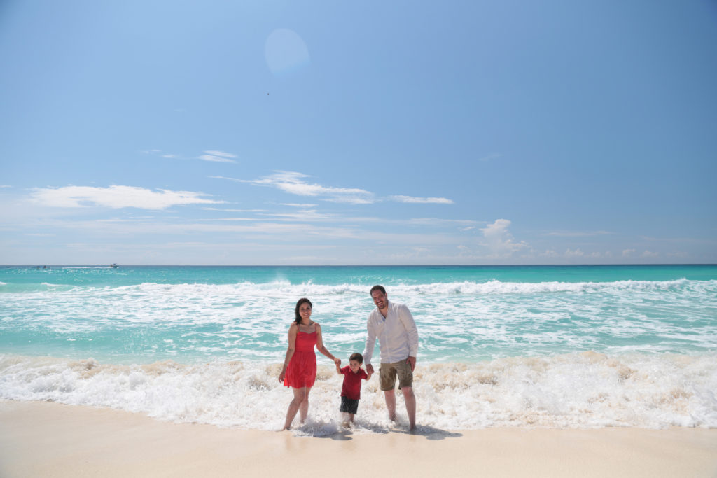 Two adults and a child hold hands while standing in the surf of waves at a beach.