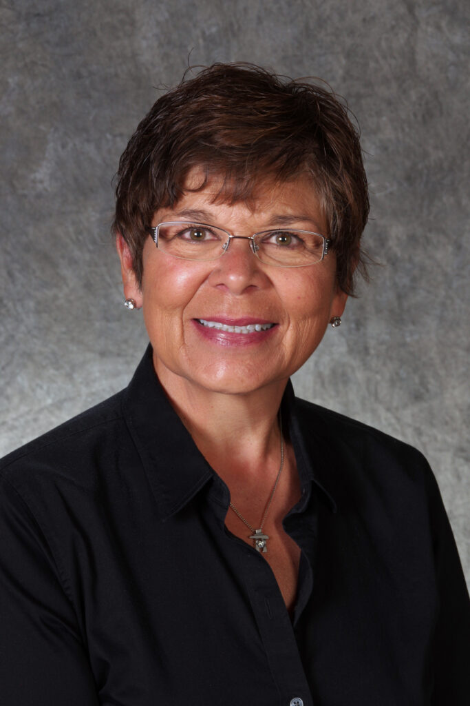 A headshot of a person with short, brown hair, glasses and a black shirt.