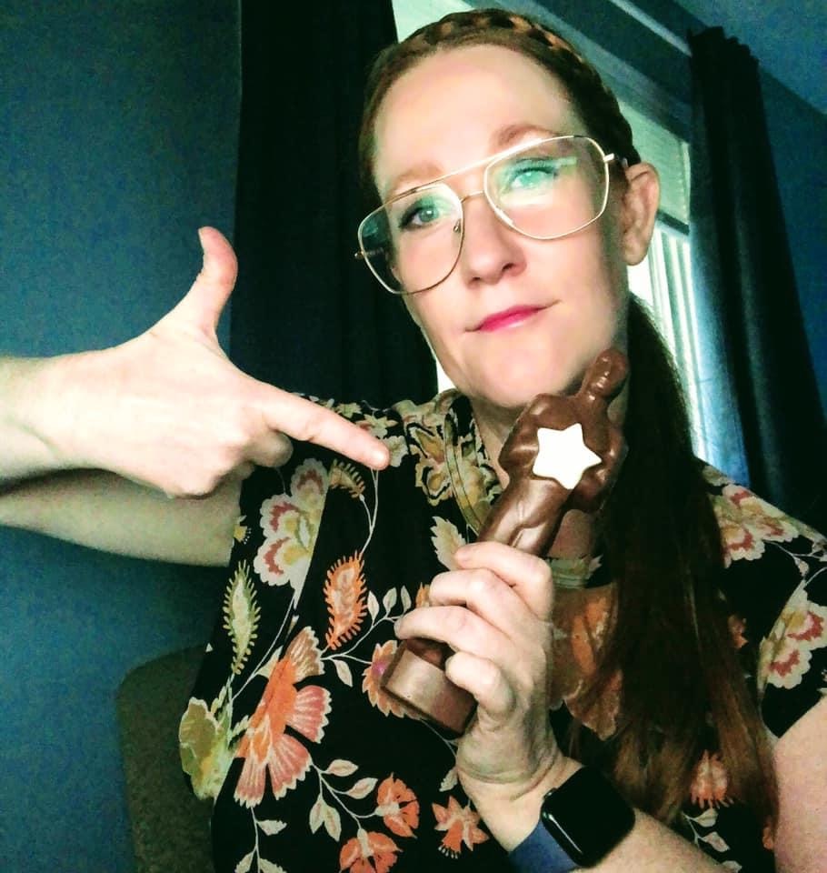 Person looks at the camera while holding a chocolate Oscar and pointing at it with their other hand.