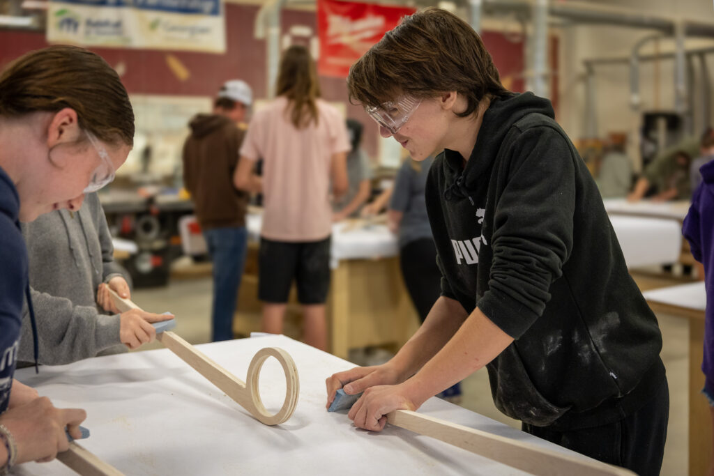 Two young students building a lacrosse stick.