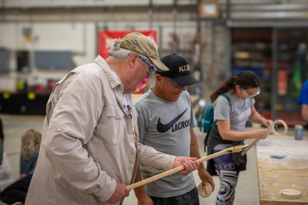 Two people making a lacrosse stick.