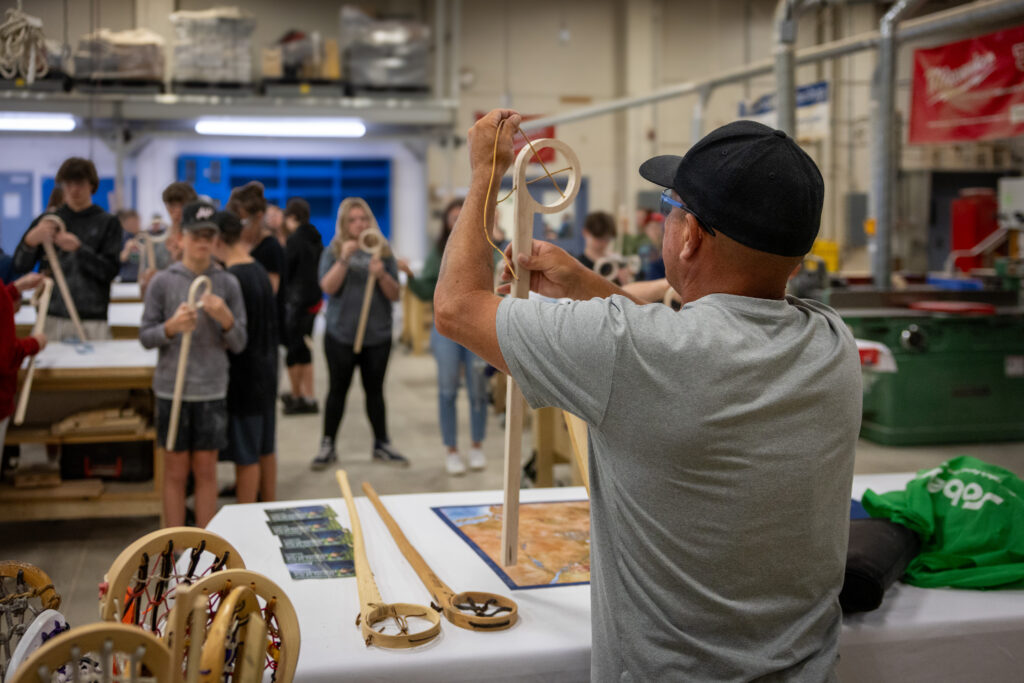 A person showing students how to build a lacrosse stick.