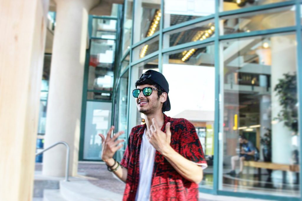 A young man standing in front of building with a lot of windows, lifting his hands up and smiling