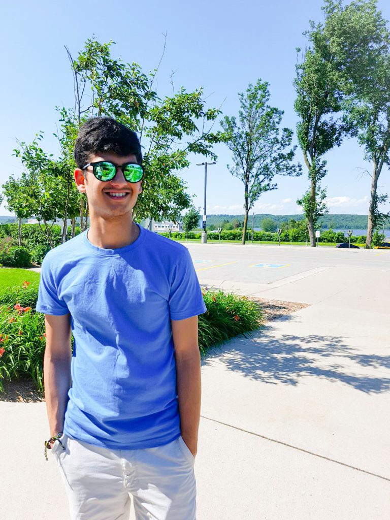 A young man standing outside, wearing sunglasses