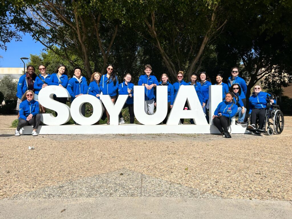 A group of students wearing blue jackets stand beside a white sign that says "Soy UAL" in Almeria, Spain.