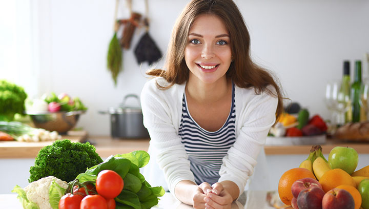 A person in a kitchen setting leaning over a counter with fresh fruit and veggies next to them