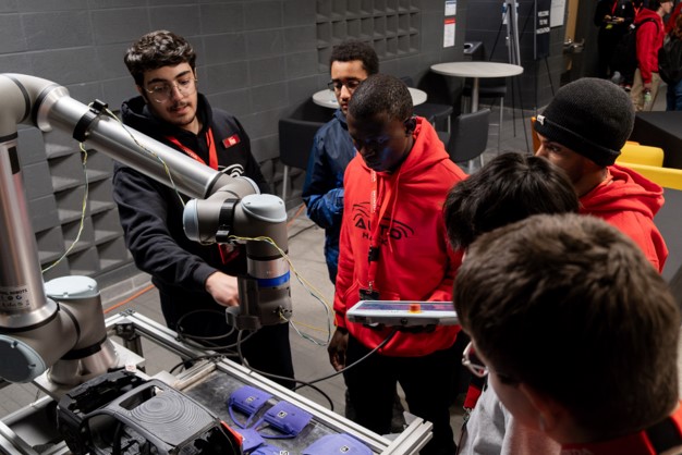 Students gathered around a collaborative robotic arm during a hands-on automotive technology demonstration.