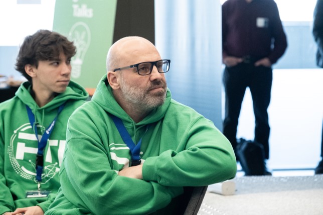 Participant in a green PTI hoodie listening during a classroom or training session, with another student seated nearby.