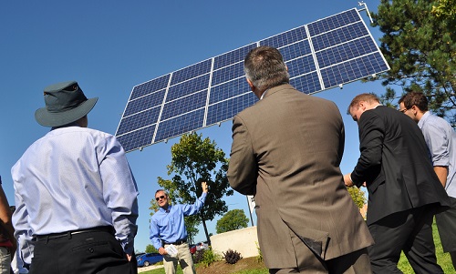 Georgian professor Dr. Ron Sky explains the benefits of having a solar array on the Owen Sound Campus. Ron Sky in background pointing at 20-unit solar array with three men in foreground listening with their backs turned from the camera.