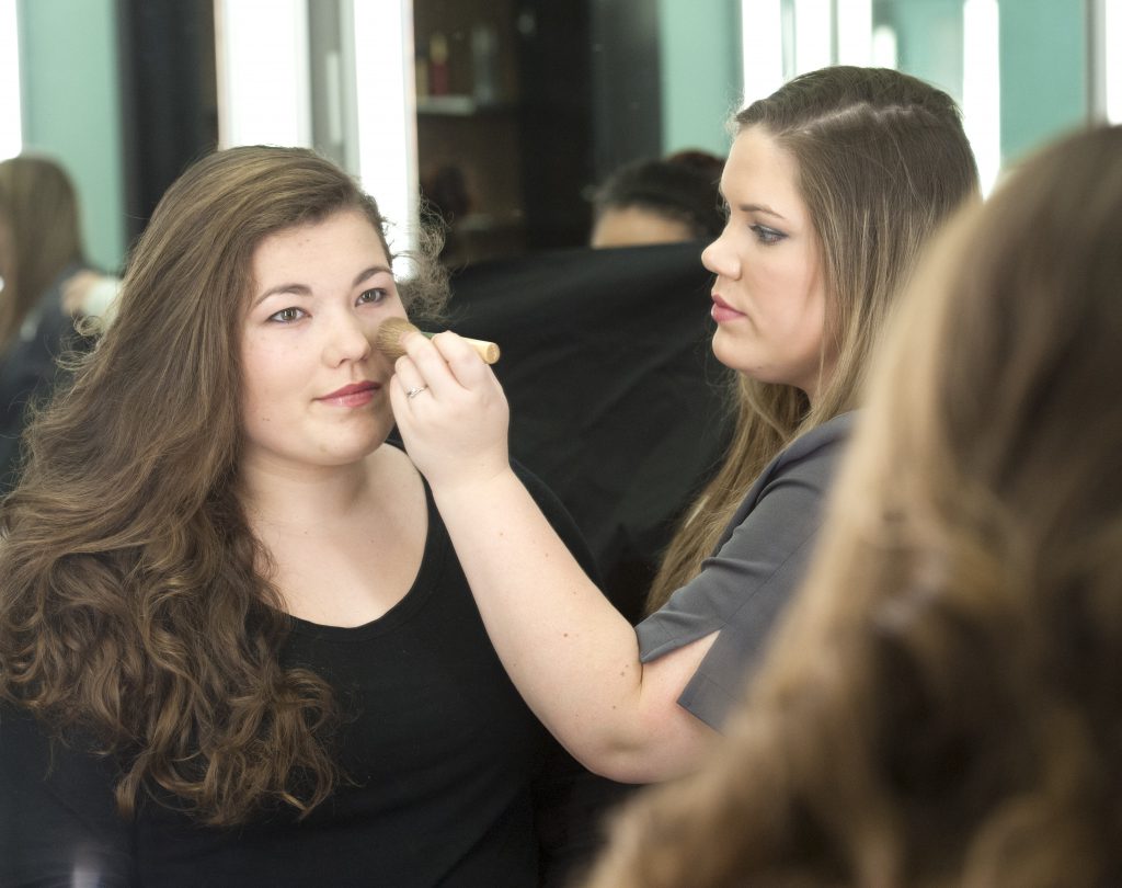 Student applying makeup to a young woman