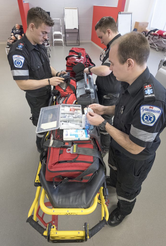 3 male paramedic students in the paramedic lab with stretcher and tools