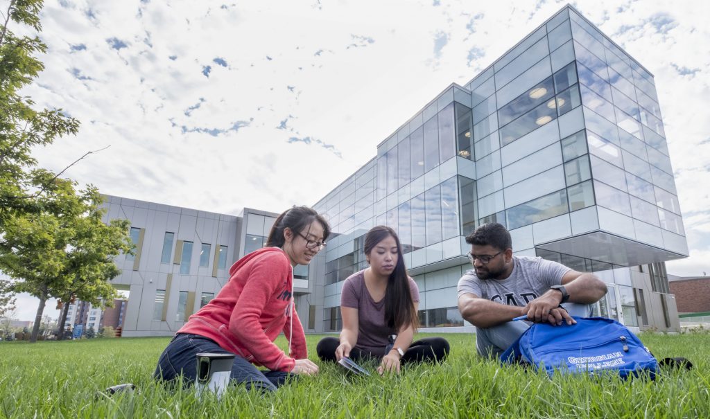 2 female and 1 male student sitting outside of the Peter B. Moore Advanced Technology Centre
