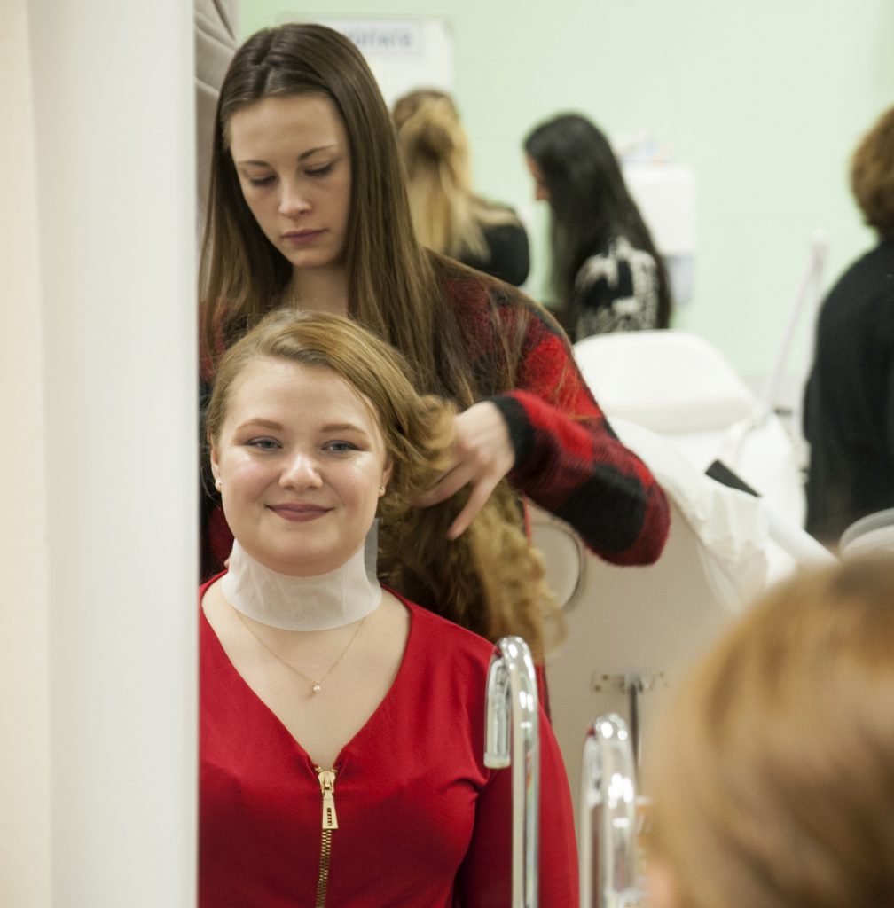 Hairstyling student doing a young woman's hair in the mirror