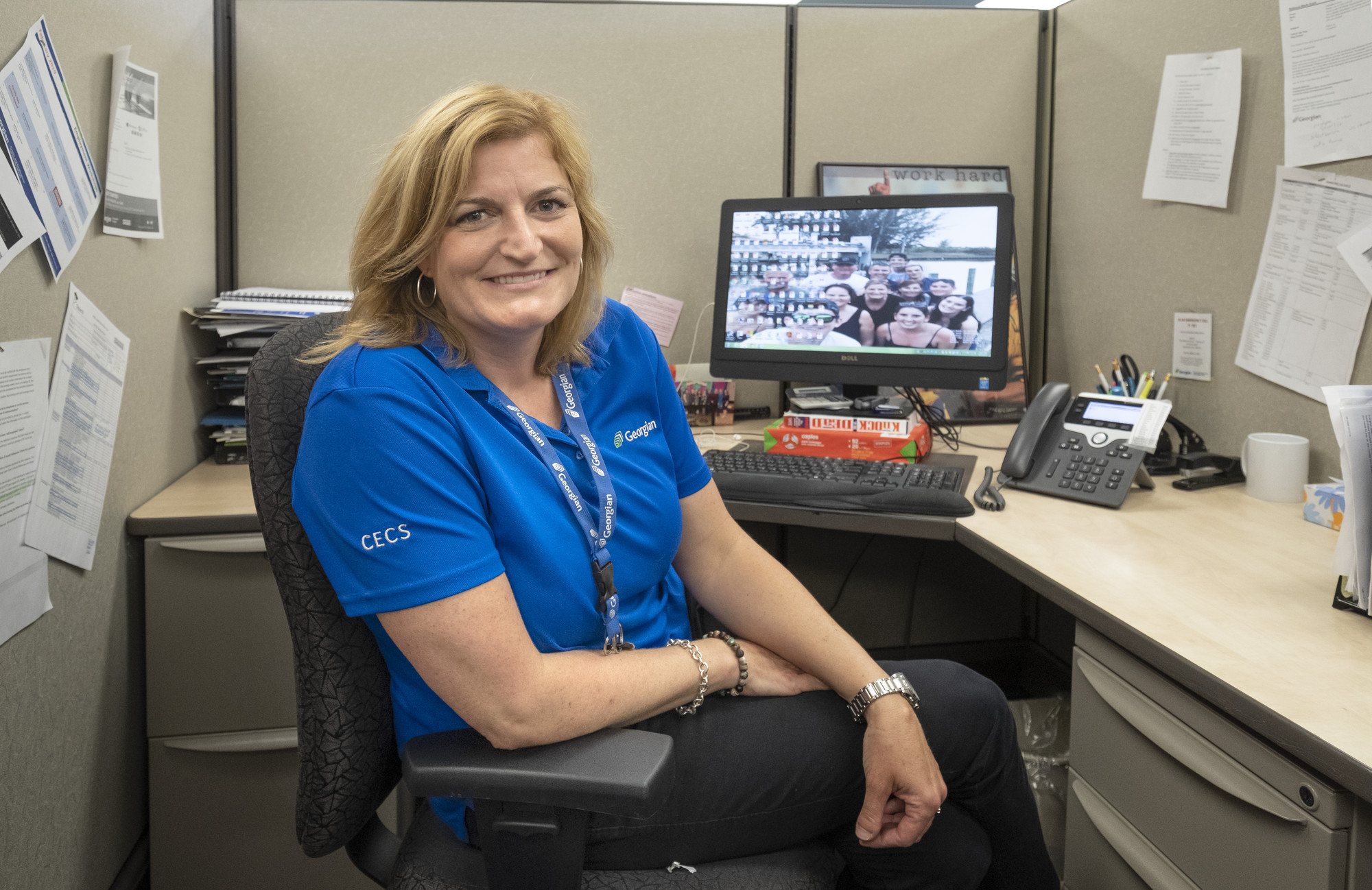 Picture of a staff member at the Orangeville Campus sitting at a computer smiling at the camera