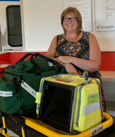 Person leans against medical equipment and smiles at the camera.