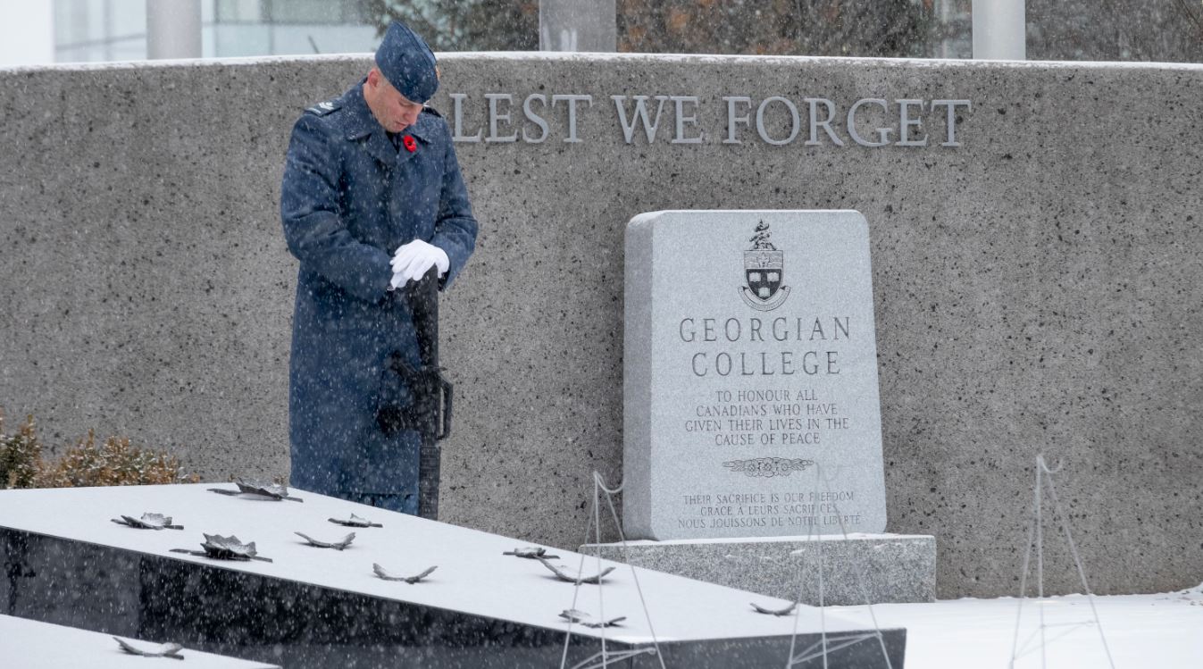Member of Honour Guard in blue military uniform stands in light snow at Georgian College Barrie Campus Cenotaph on Remembrance Day