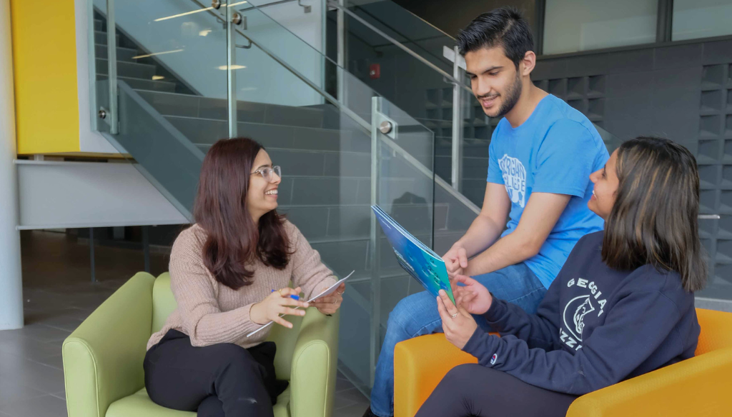 Three students are sitting on chairs at the Barrie Campus M building. Two women and one man.