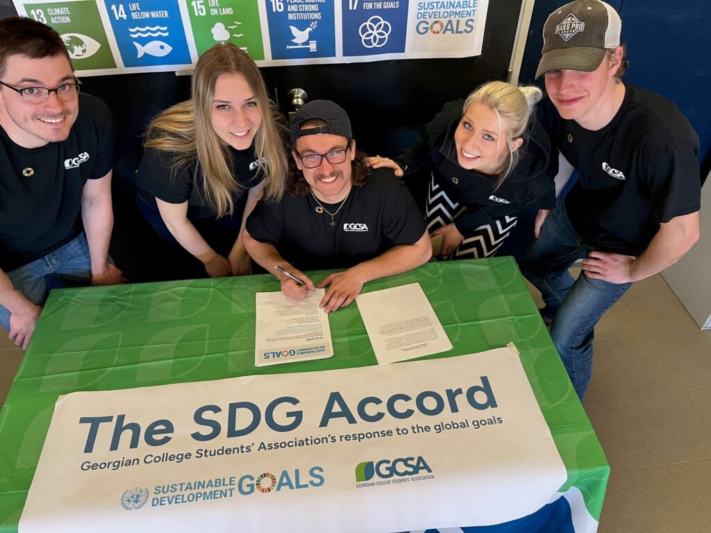 Five members from the Georgian College Students' Association (Midland) sitting at a table signing the SDG Accord.