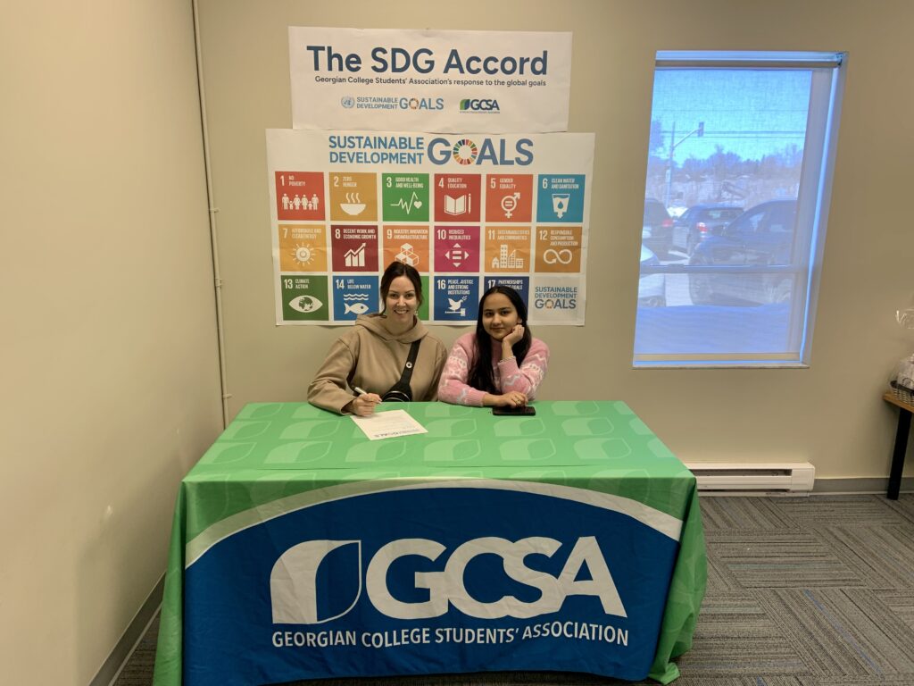 Two people sitting at a green and blue table, signing a piece of paper for the SDG Accord.