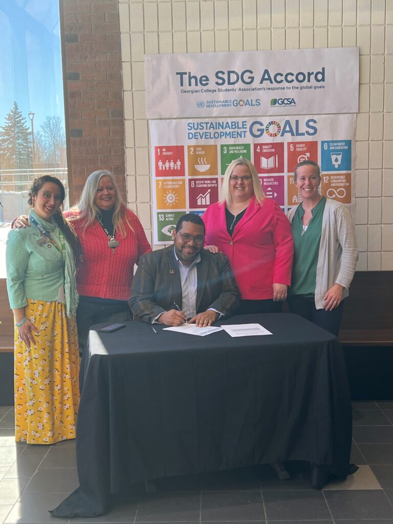 Five people surrounding a table where one person signs a paper for the SDG Accord.