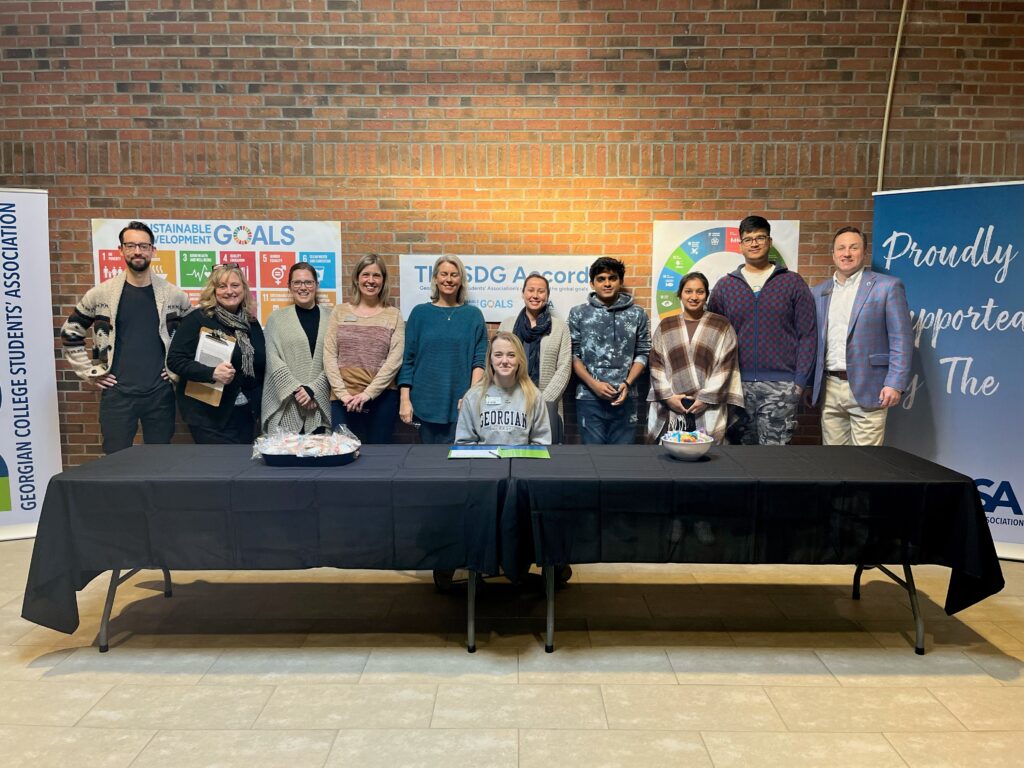 The Owen Sound Georgian College Students' Association sitting at a black table, signing the SDG Accord with banners in the background.