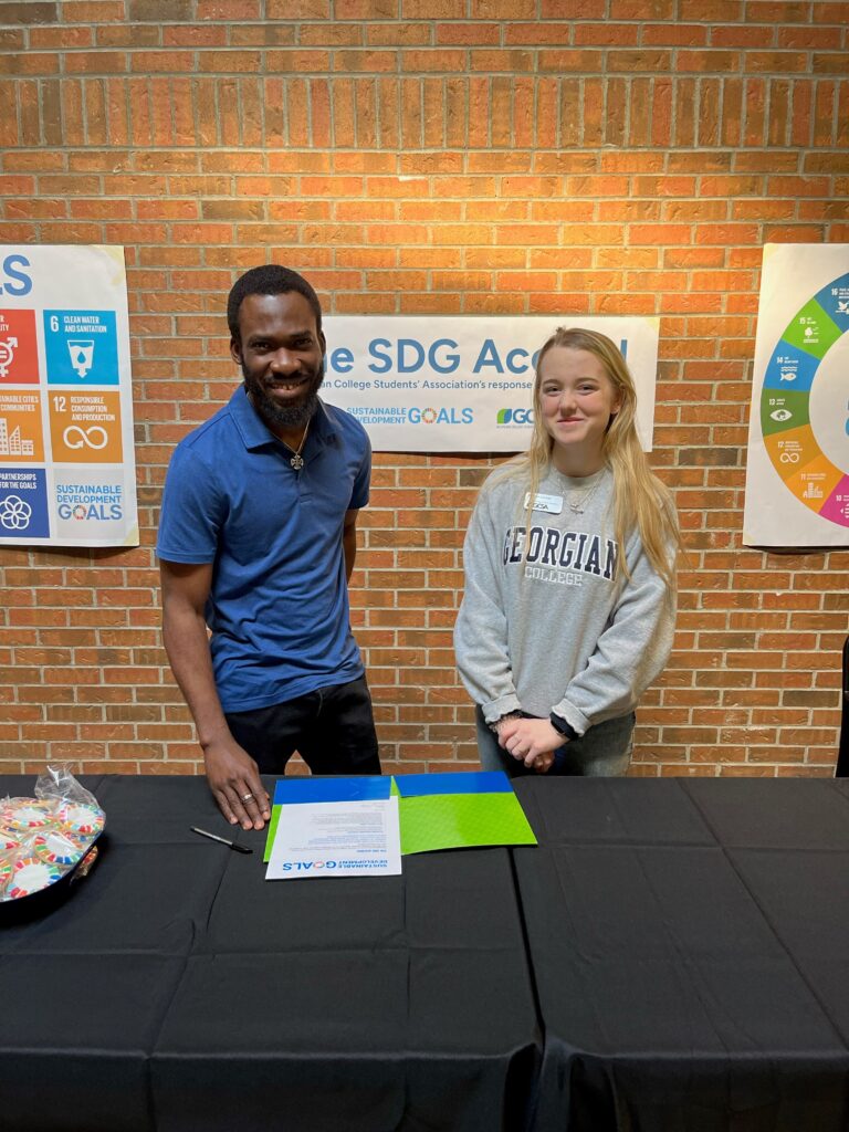 Bankole Faloye (left) and Owen Sound GCSA President Madison Lindsay (right) standing at a table signing the SDG Accord.