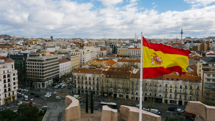 Photo of cityscape with Spanish flag in foreground.