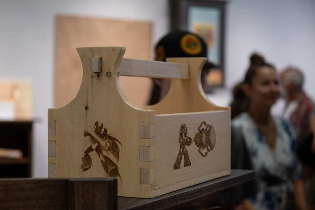 A student-made toolbox is in the foreground with people faded in the background at the 2025 student cabinetmaking exhibit.