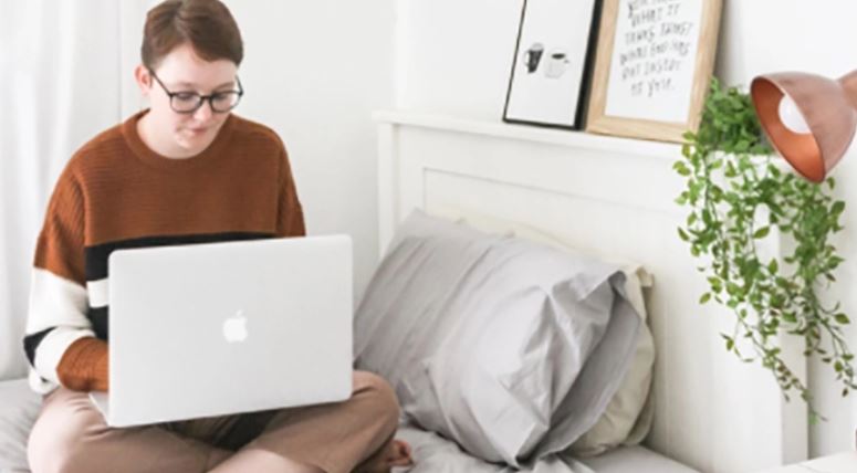 Student works on laptop while sitting on bed 