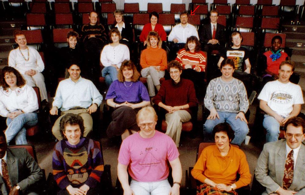 Four rows of people sit in a lecture hall and smile for a photo.