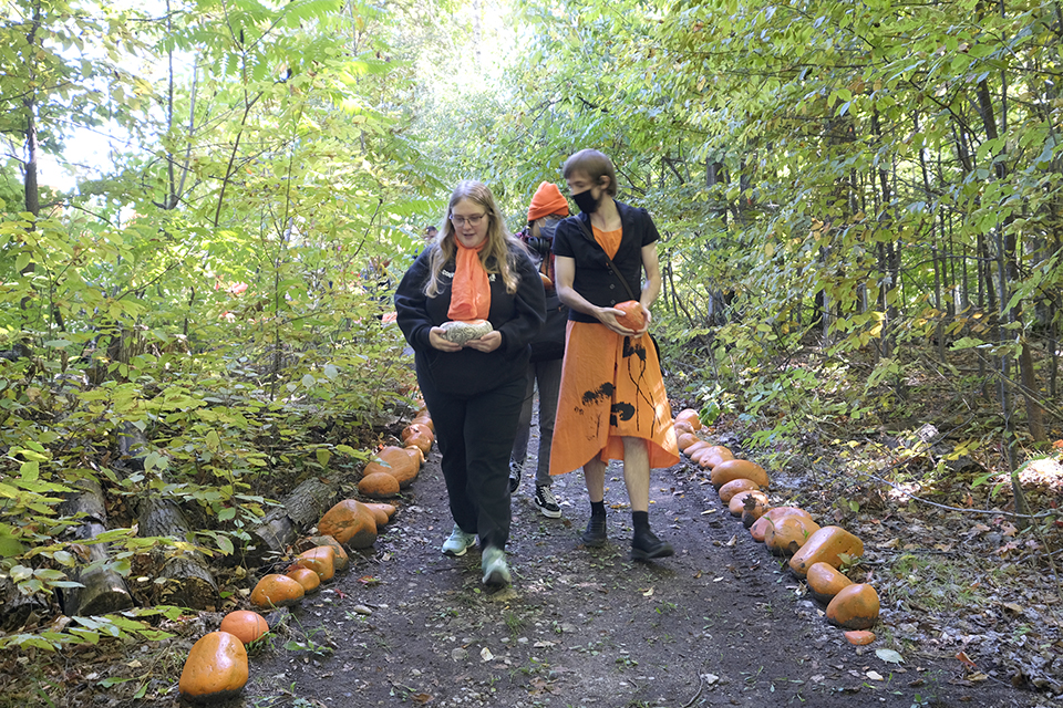 People wearing orange walk down a forest trail with orange rocks placed along either side of it.