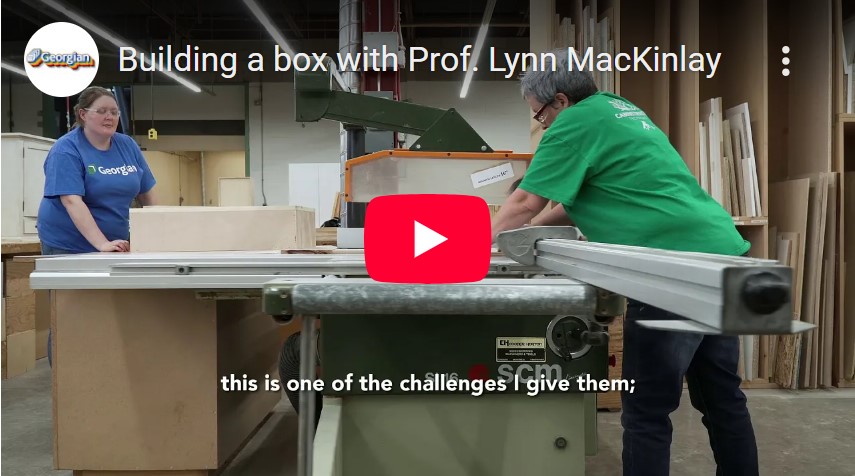 A screen grab of a YouTube video of Professor Lynn MacKinlay and a student working on a project int eh shop space. There's a YouTube button overlay and some of the closed captioning on this screen grabs says, "...this is one of the challenges I give them;".