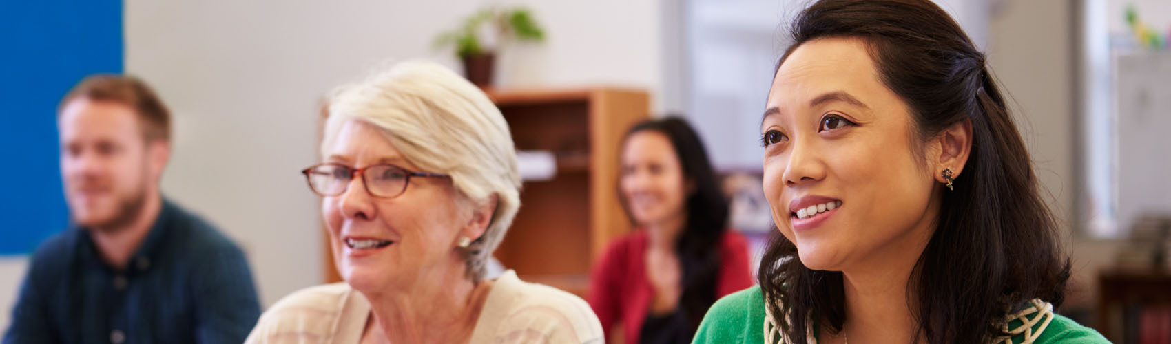 A mature woman and younger woman listening in a classroom with other students in the background