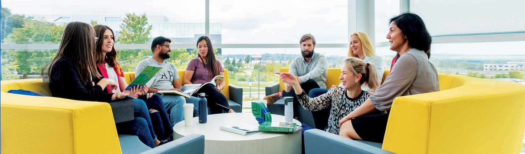 Students sitting in the Peter B. Moore Advanced Technology Centre near the windows on yellow couches