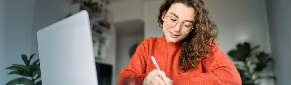 Woman writes notes in front of her laptop
