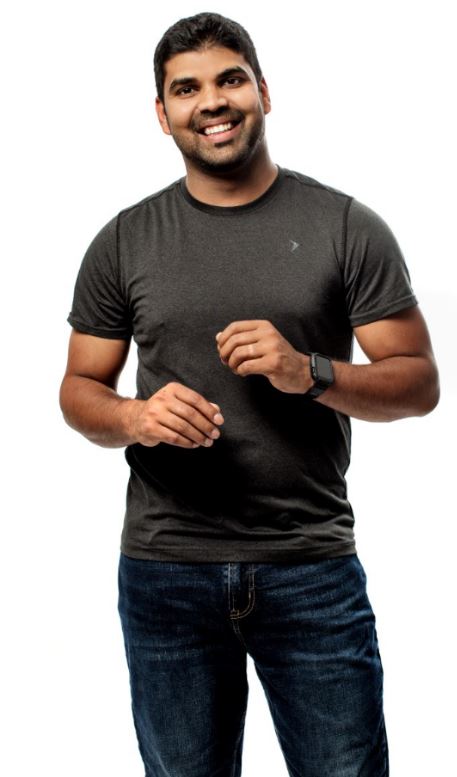 A person stands against a white backdrop and smiles at the camera.